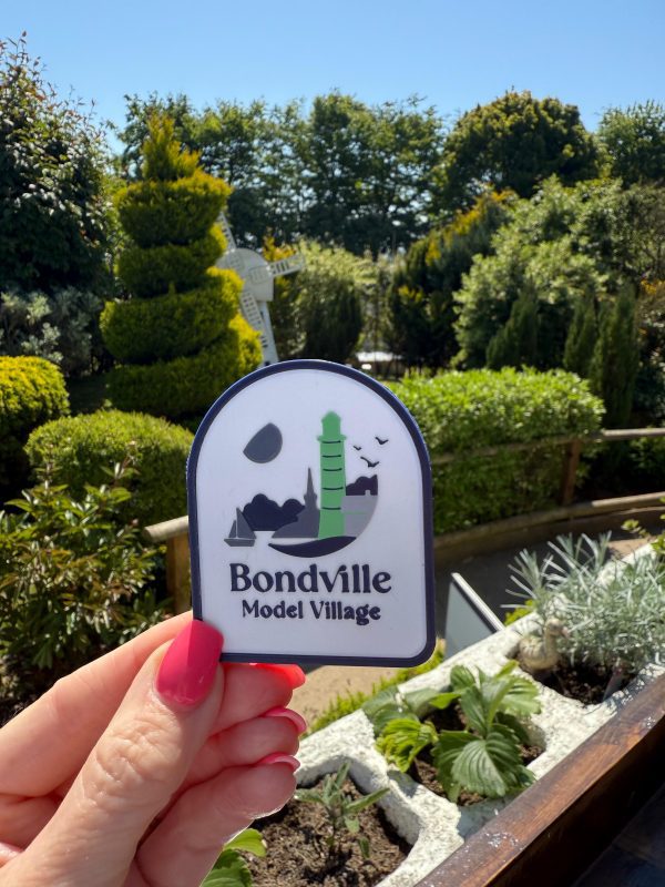 Hand holding Bondville Model Village logo fridge magnet outdoors